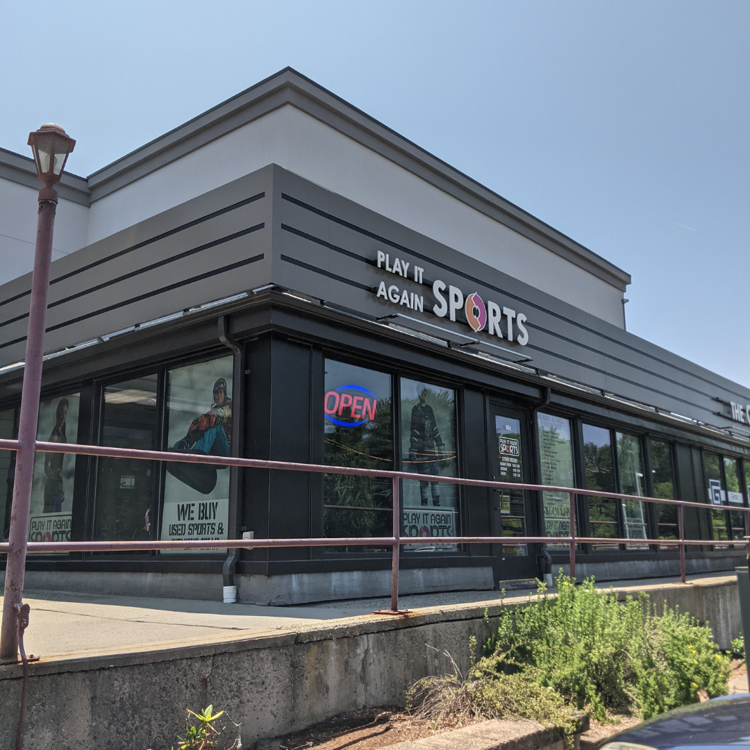 Front of store of Play It Again Sports Stoneham, a gray building with PIAS branding and graphics